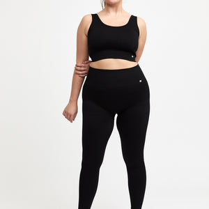träningskläder i svart från Drop Of Mindfulness. Kvinna bär ribbade svarta tights och sport-bh med bredare band.