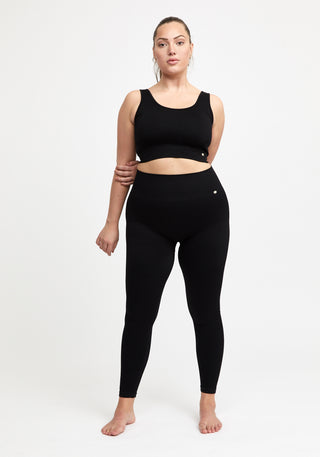 träningskläder i svart från Drop Of Mindfulness. Kvinna bär ribbade svarta tights och sport-bh med bredare band.